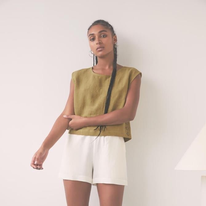 Model wears a boxy cropped olive colored tank top with a row of buttons down each side. Designed by Eve Gravel and made in Montreal, Canada.
