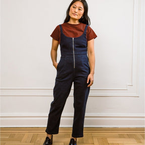 A model wears a dark denim jumpsuit with adjustable straps and a front zipper. The Claudia Jumpsuit in Dark Indigo is designed by Loup and made in New York City, USA.