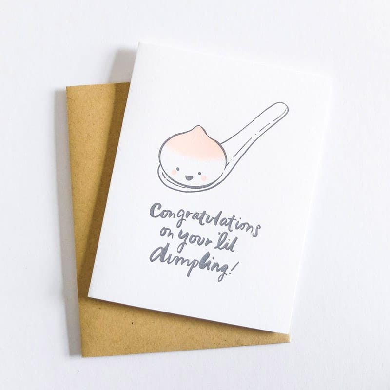 White card with the image of a smiling dumpling in a spoon. Text on the bottom reads: "CONGRATULATIONS ON YOU 'LIL DUMPLING!" Designed by Hello! Lucky and made in San Francisco, CA. Measures 4.25 x 5.5 inches.