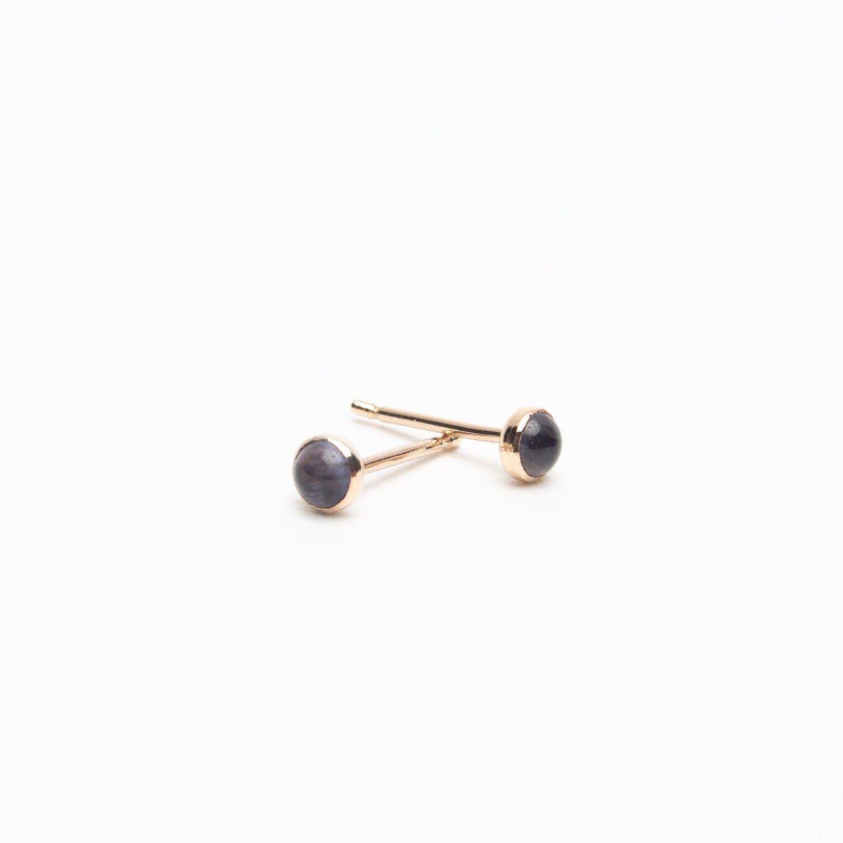 A blue/purple Iolite stone encased in gold-fill with a gold-fill earring post. The Gold-fill Iolite Studs are designed and handcrafted by Deivi Arts Collective in Vancouver, Canada.