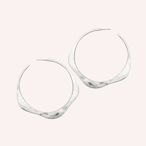 A sterling silver hoop earring in a wave design with a hand hammered texture and sterling silver earring posts. The large Doble Hoop Earrings are designed and handcrafted in Portland, Oregon.