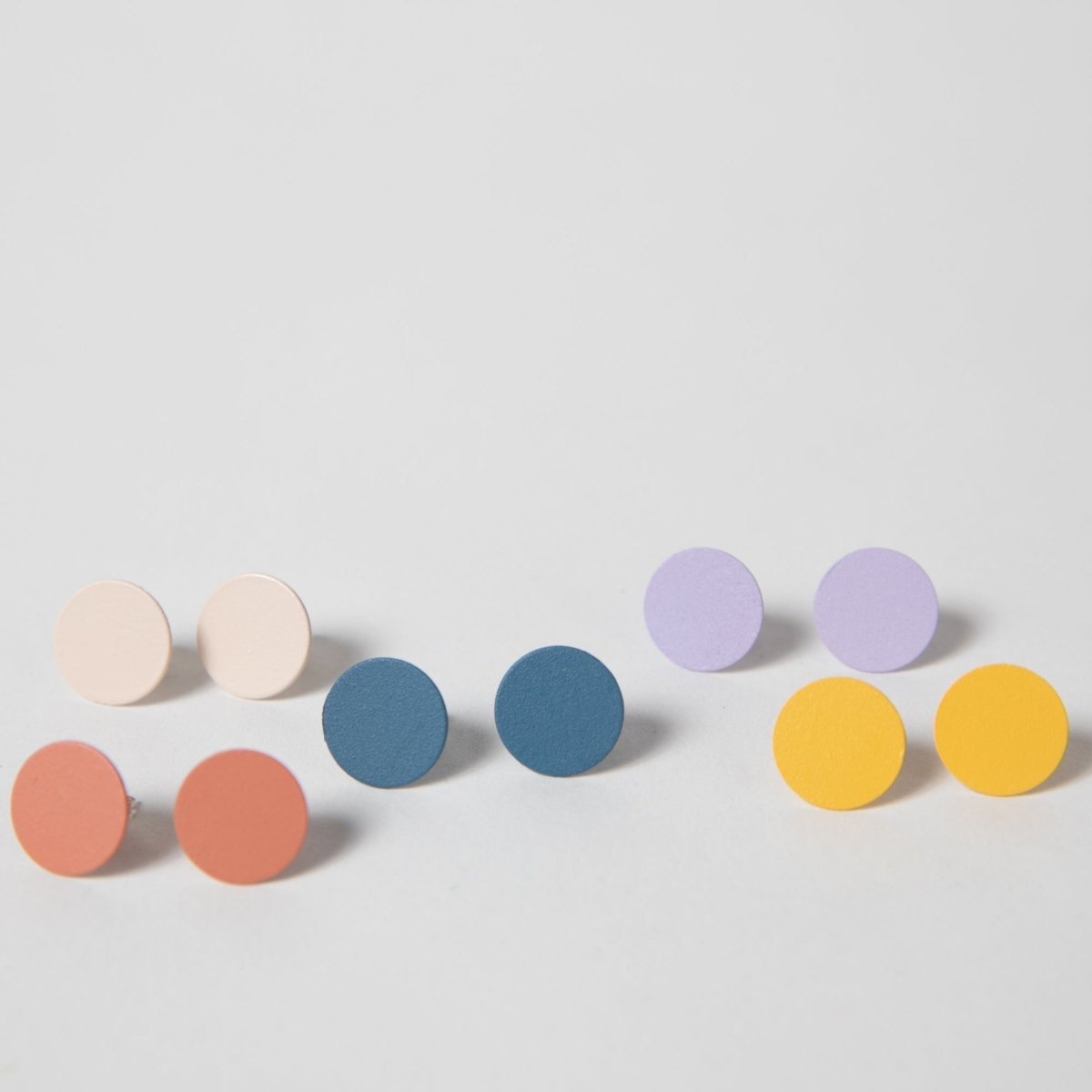 An array of flat stud earrings in Cream, Coral, Cobalt, Lilac and Marigold. The Dot earrings are designed and crafted by Pretti.cool in Houston, Texas.