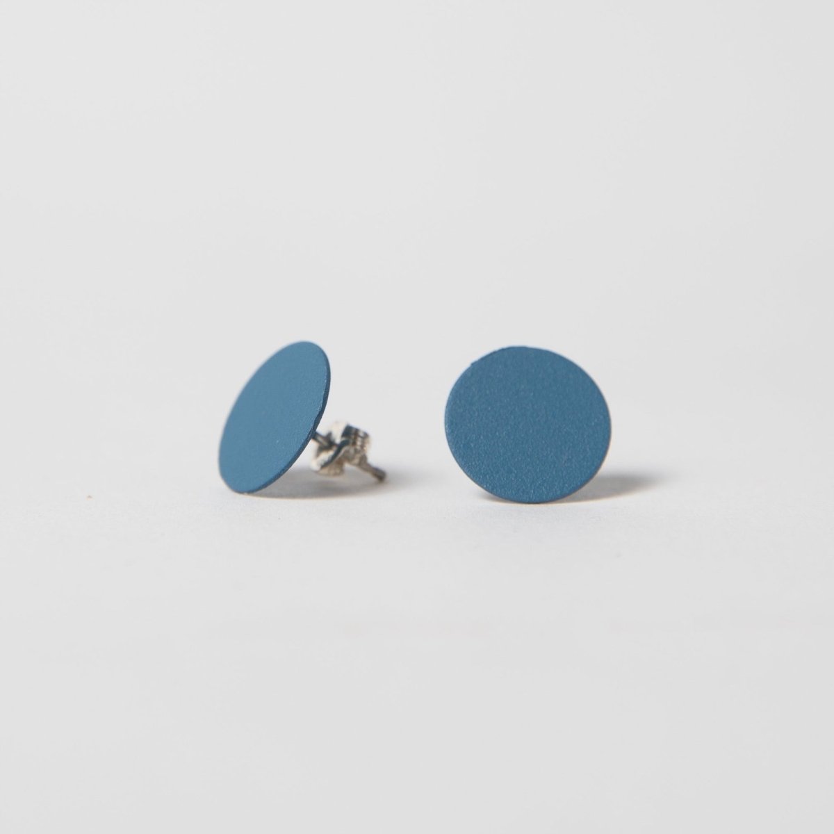 A round flat stud earring in dark blue. The Dot Earrings in Cobalt are designed and crafted by Pretti.cool in Houston, Texas.