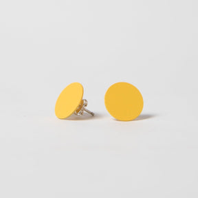 A round flat stud earring in yellow. The Dot Earrings in Marigold are designed and crafted by Pretti.cool in Houston, Texas.