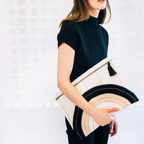Model holds oversized square pouch with a cross-stitched concentric pattern in neutral colors. Includes zipper with a black tassel. Designed by Anchal in Louisville, Kentucky and handmade in Ajmer, India.