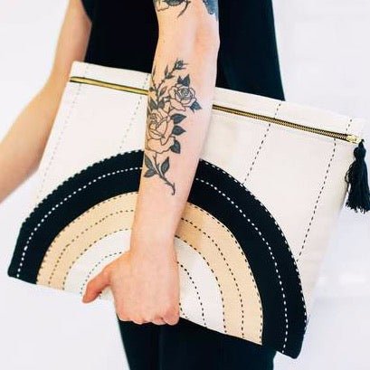 Model holds oversized square pouch with a cross-stitched concentric pattern in neutral colors. Includes zipper with a black tassel. Designed by Anchal in Louisville, Kentucky and handmade in Ajmer, India.