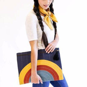Model holds oversized square pouch with a cross-stitched concentric pattern in various colors. Includes zipper with a black tassel. Designed by Anchal in Louisville, Kentucky and handmade in Ajmer, India.