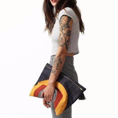 Model holds oversized square pouch with a cross-stitched concentric pattern in various colors. Includes zipper with a black tassel. Designed by Anchal in Louisville, Kentucky and handmade in Ajmer, India.