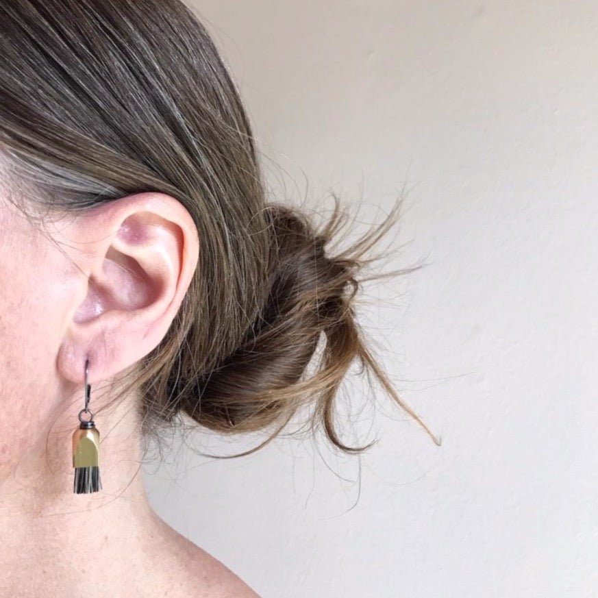 Model wears grey horsehair fringe earrings with a dome shaped brass cap and oxidized sterling silver leverback. Designed and made by Boet in Portland, Oregon.