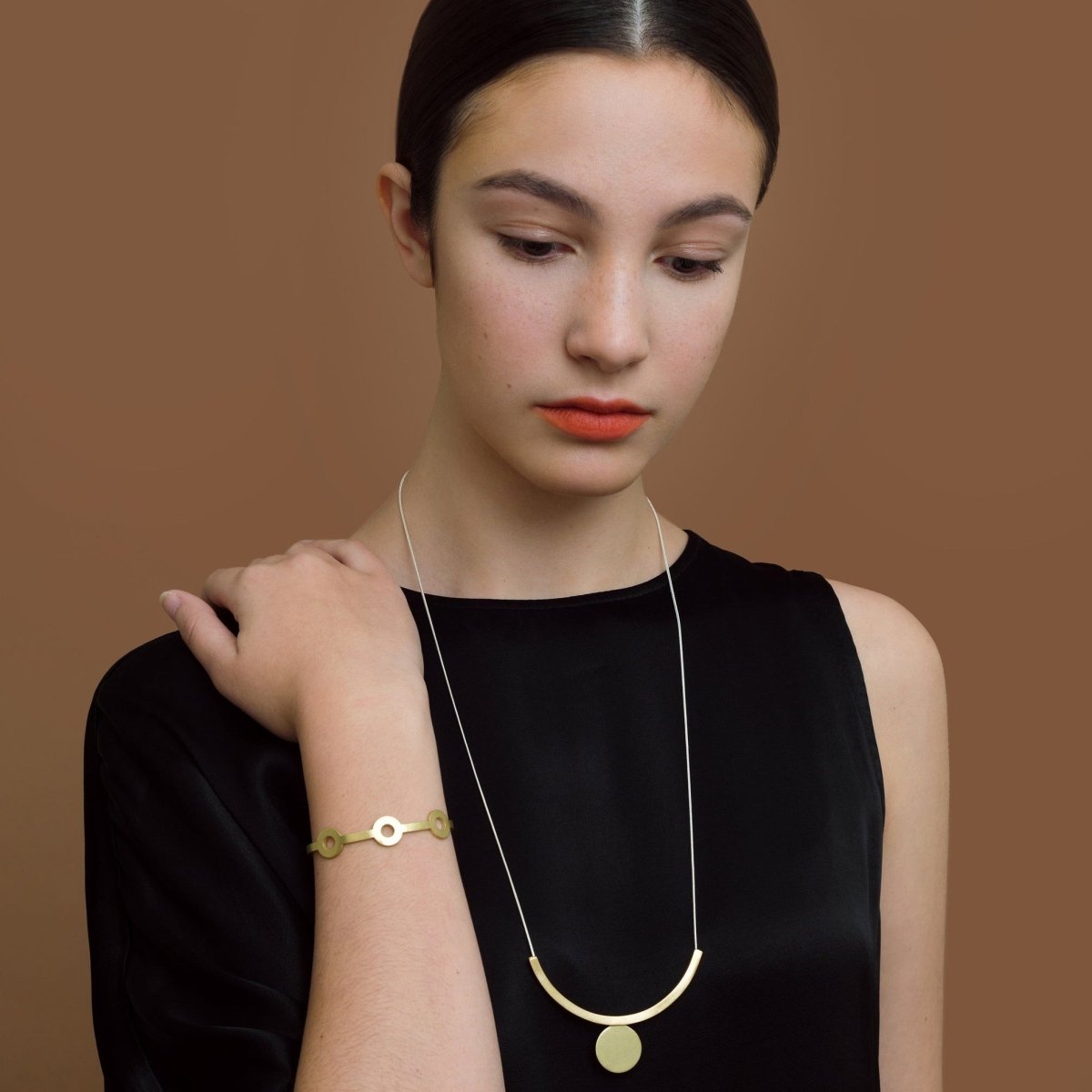 A silver chain necklace with a rounded brass and circle bar focal piece. The Floating Necklace is designed and handcrafted by Natalie Joy in Portland, Oregon.