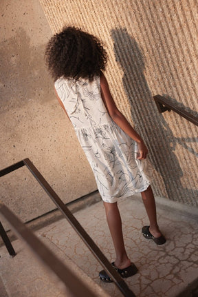 A model shows the backside of a white sleeveless dress with a route neckline and black line illustrations. The Galatee Dress in Cream & Black is designed and made by Eve Gravel in Montreal, Canada.