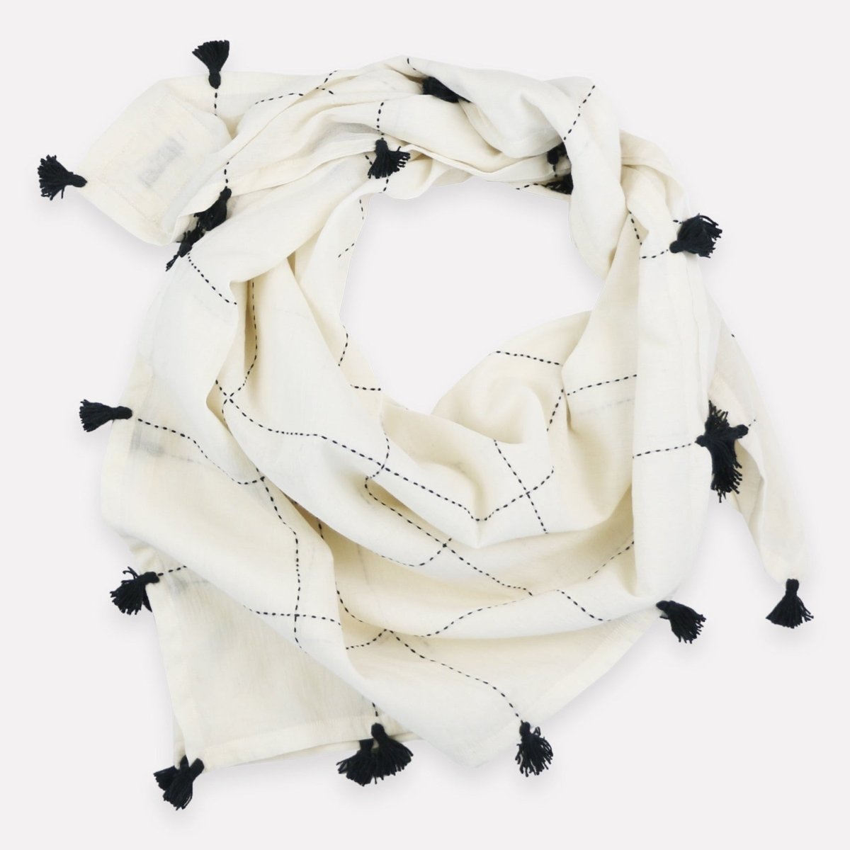 Cream colored scarf with black stitching and black tassels around the border. The Grid Scarf in Bone with Tassels in designed by Anchal in Louisville, Kentucky and handmade in Ajmer, India.