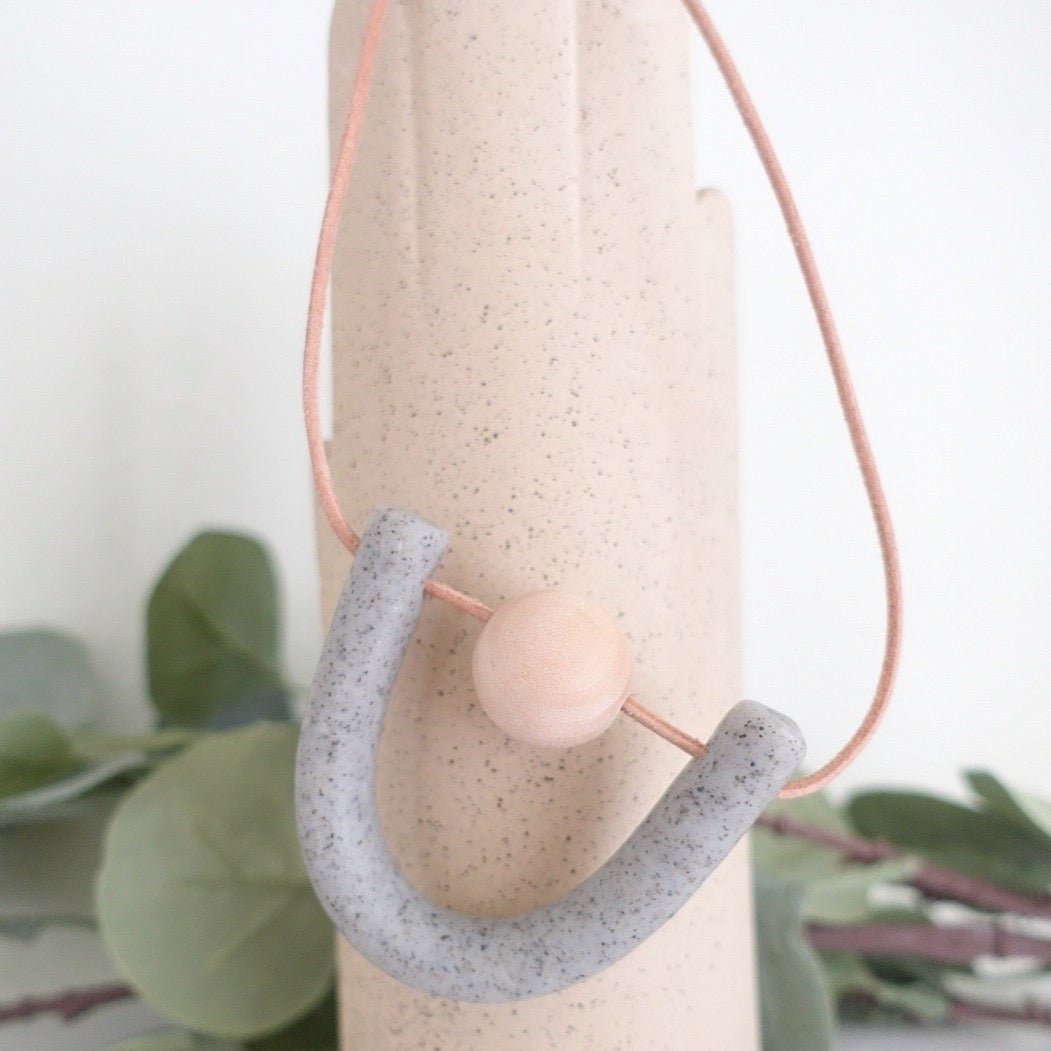 U-shaped focal piece made of polymer clay  with a natural wood ball suspended by orange leather cord. Made by Hey Moon Designs in Los Angeles, CA.