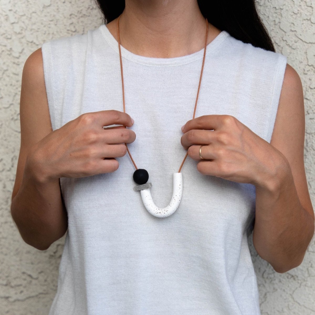 Asymmetrical white speckle U + triangle granite disc + black orbit made of polymer clay and orange leather cord worn over a white tank top. Made in Los Angeles, California by Hey Moon Designs. 