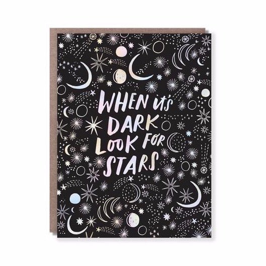 Front of card reads: "WHEN IT'S DARK LOOK FOR STARS" with white patterned constellations against a black background. Comes with a brown Kraft envelope. Designed by Hello! Lucky and made in San Francisco, CA. Measures 4.25 x 5.5 inches.