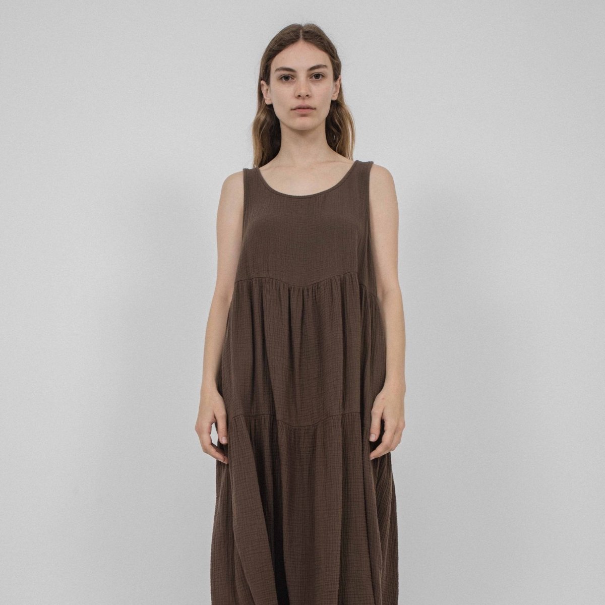 A model wears a sleeveless loose fitting dress with two tiers of fabric that form the bottom portion of the dress. The Harlow Dress on Cocoa is designed and made by Corinne Collection in Los Angeles, CA.