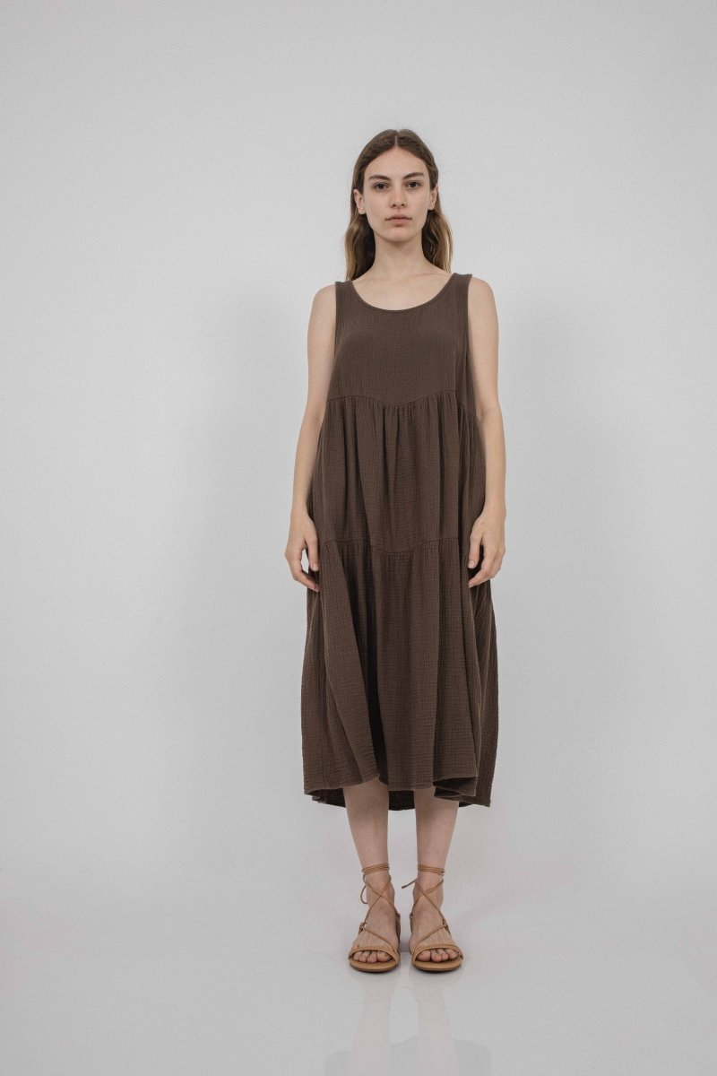 A model wears a sleeveless loose fitting dress with two tiers of fabric that for the bottom portion of the dress. The Harlow Dress on Cocoa is designed and made by Corinne Collection in Los Angeles, CA