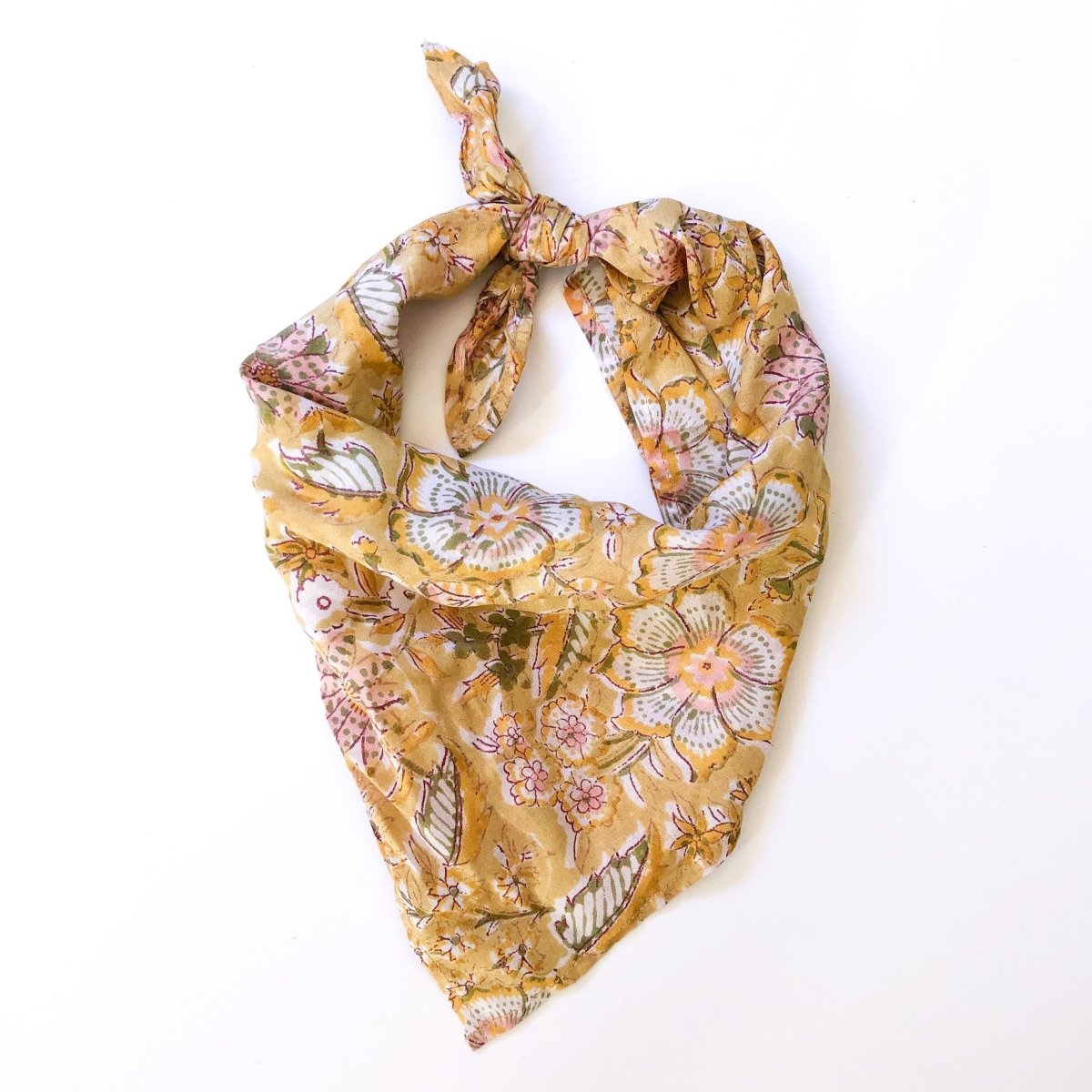 A yellow, pink, white and green floral patterned bandana, folded over and tied in a knot. Block printed by hand, the Harlowe Bandana from Maelu is designed in Portland, Oregon ad handmade in India.