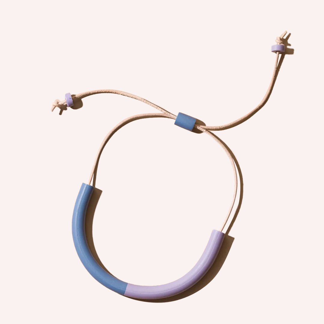 A U-shaped polymer clay necklace in a light blue and purple color with a tan leather strap. The Two-tone Harper Mini Necklace in Stone and Lilac is designed by Little Pieces Jewelry and made in Los Angeles, CA.