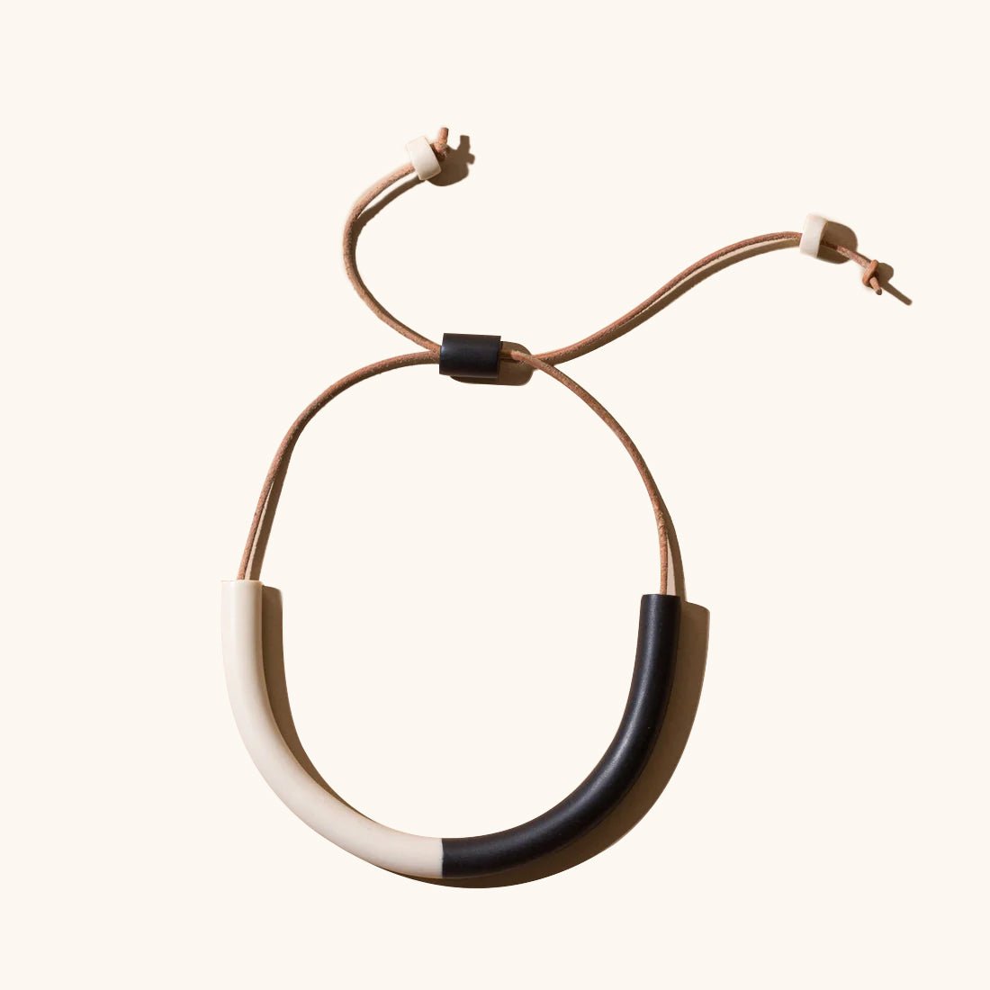 A U-shaped polymer clay necklace in an off white and black color with a tan leather strap. The Two-tone Harper Mini Necklace in Black and Cream is designed by Little Pieces Jewelry and made in Los Angeles, CA.
