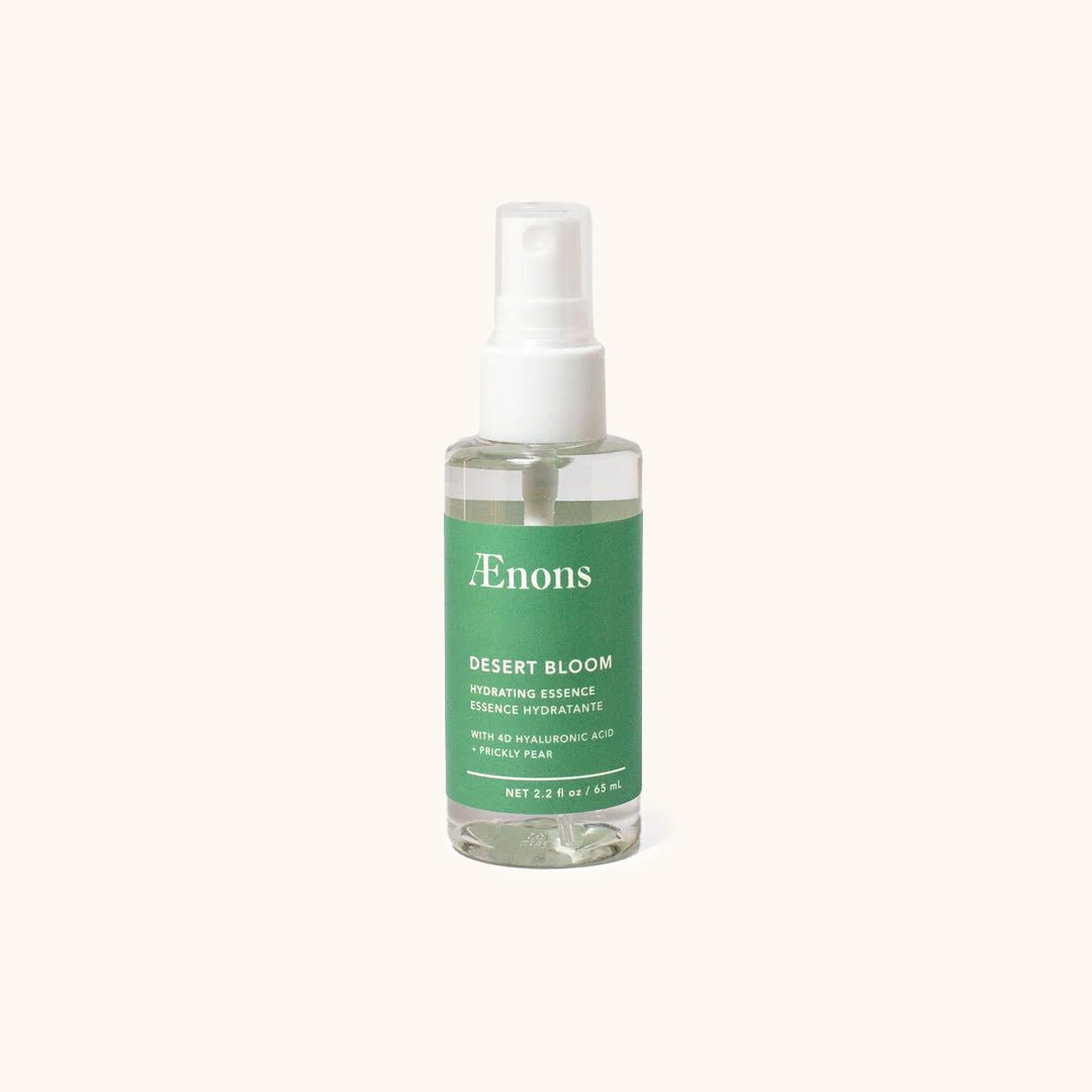 A clear spray bottle with a green label holds a clear hydrating toner. The Desert Bloom Hydrating Essence Face Mist is crafted by Aenons and made in Los Angeles, CA.