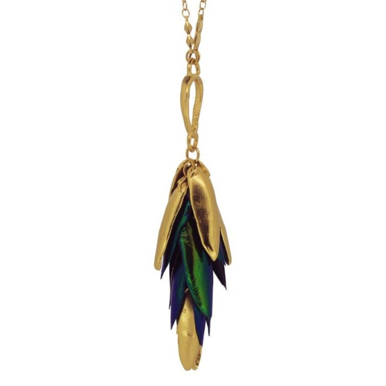Closeup of the I Can See the Light Necklace by designer Lingua Nigra. Brass chain connected to brass wing-like shapes and blue and green beetle wings.
