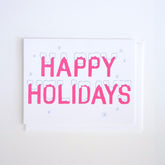 Neon pink text reads: "HAPPY HOLIDAYS" with a mantle of freshly fallen snow and petite stars against a white background. Made with recycled paper by Banquet Atelier in Vancouver, British Columbia, Canada.