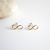 A gold tone stud earring in the infinity symbol. The Infinity Stud Earring is designed by Hooks and Luxe and handcrafted in Jackson Heights, NY.