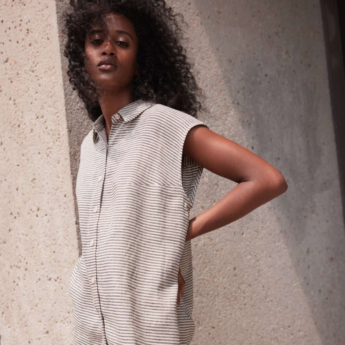 A model wears a sleeveless button up with a gray and cream stripe pattern. Designed by Eve Gravel and made in Montreal, Canada.