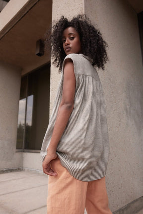 A model wears a sleeveless button up with a gray and cream stripe pattern. Designed by Eve Gravel and made in Montreal, Canada.