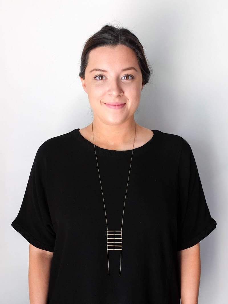 Long, cast-bronze betsy & iya Jalisco necklace, shown on a smiling model wearing a black tunic.