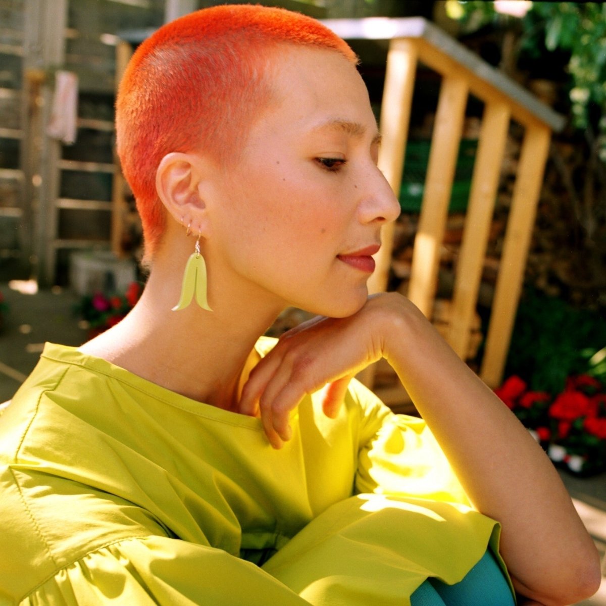 A model wears green arched shaped earrings with sterling silver ear wire. The Joined Feathers Mini Earrings in Sour Apple are designed and crafted by Warren Steven Scott in Canada.