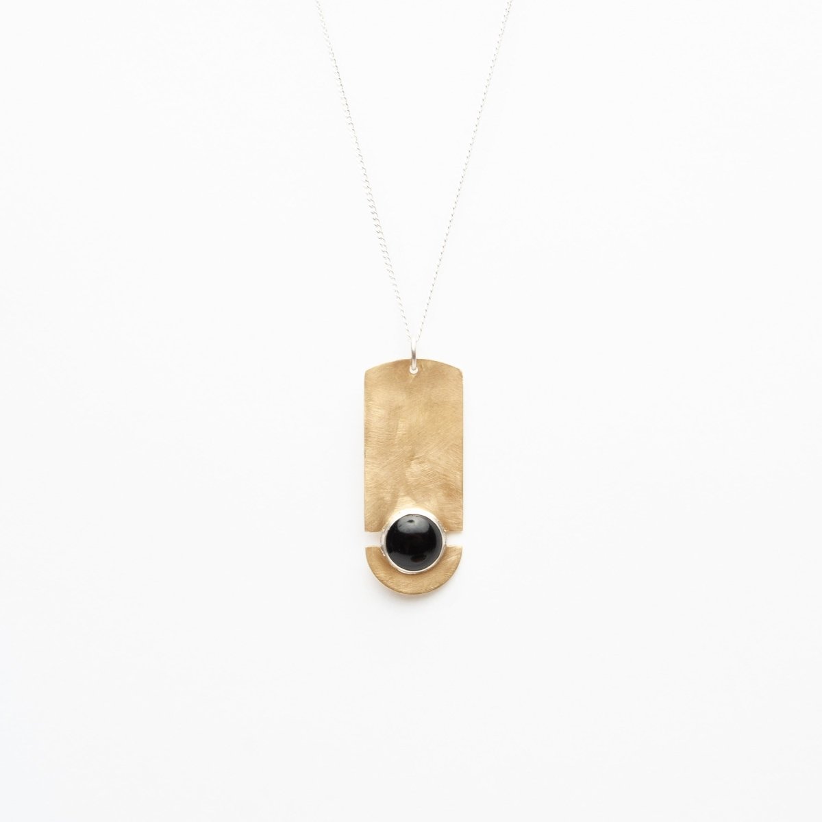 Elongated pendant necklace made of brass with a Black Onyx stone set between two slits and a rounded bottom edge.  Pendant hangs from a sterling silver chain. Designed by Kari Phillips in Portland, Oregon.
