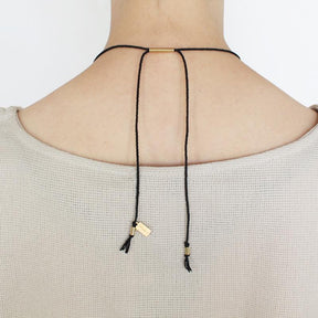 The betsy & iya Kanssa necklace, photographed from the back of a model, with the black Japanese cotton rope adjusted to a short length, brass tubing accents, and black cotton fringe.