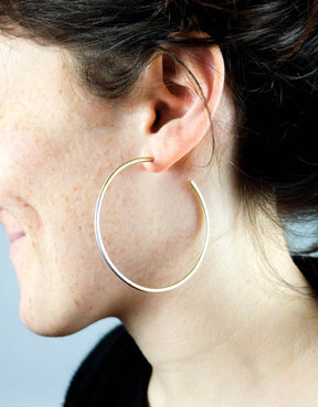 Minimalist, lightweight, mixed metal hoops of 14k yellow gold and sterling silver hand-forged wire, with 14k gold earring posts. Size large, two and one-eighth inches in diameter, worn by a model with brown hair pulled into an updo.
