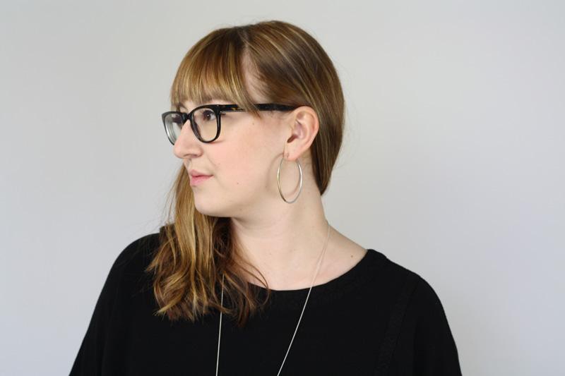 Large sterling silver and brass betsy & iya Koa hoop earrings, pictured on the profile of a model with sandy-blond bangs and glasses.