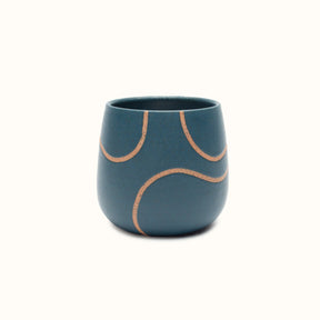 A handless mug in a blue matte finish with a single squiggle design in raw speckled clay. The Tea Cup with Single Squiggle in Blue is designed by Kohai Ceramics and handmade in Portland, OR.