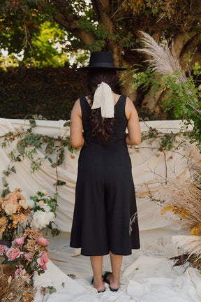 Model shows back side of relaxed sleeveless midi-length jumpsuit with pockets in the color True Black. The Lakeside Jumpsuit is designed by Mien and made in Los Angeles, CA.