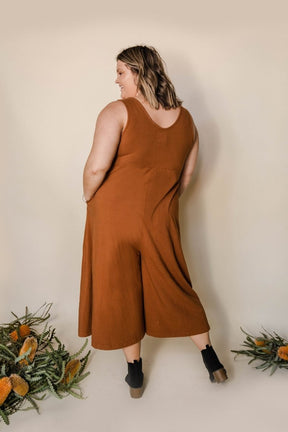 Model shows the back side of relaxed sleeveless midi-length jumpsuit with pockets in the color Saddle Brown. The Lakeside Jumpsuit is designed by Mien and made in Los Angeles, CA.