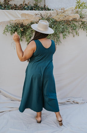 Model shows back side of relaxed sleeveless midi-length jumpsuit with pockets in the color Rich Teal. The Lakeside Jumpsuit is designed by Mien and made in Los Angeles, CA.