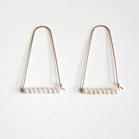 A wide gold tone arch shaped earring with a bar of freshwater pearls at the bottom. The Large Mountain Hoop earrings with Freshwater Pearls are designed by Hooks and Luxe handcrafted in Jackson Heights, NY.