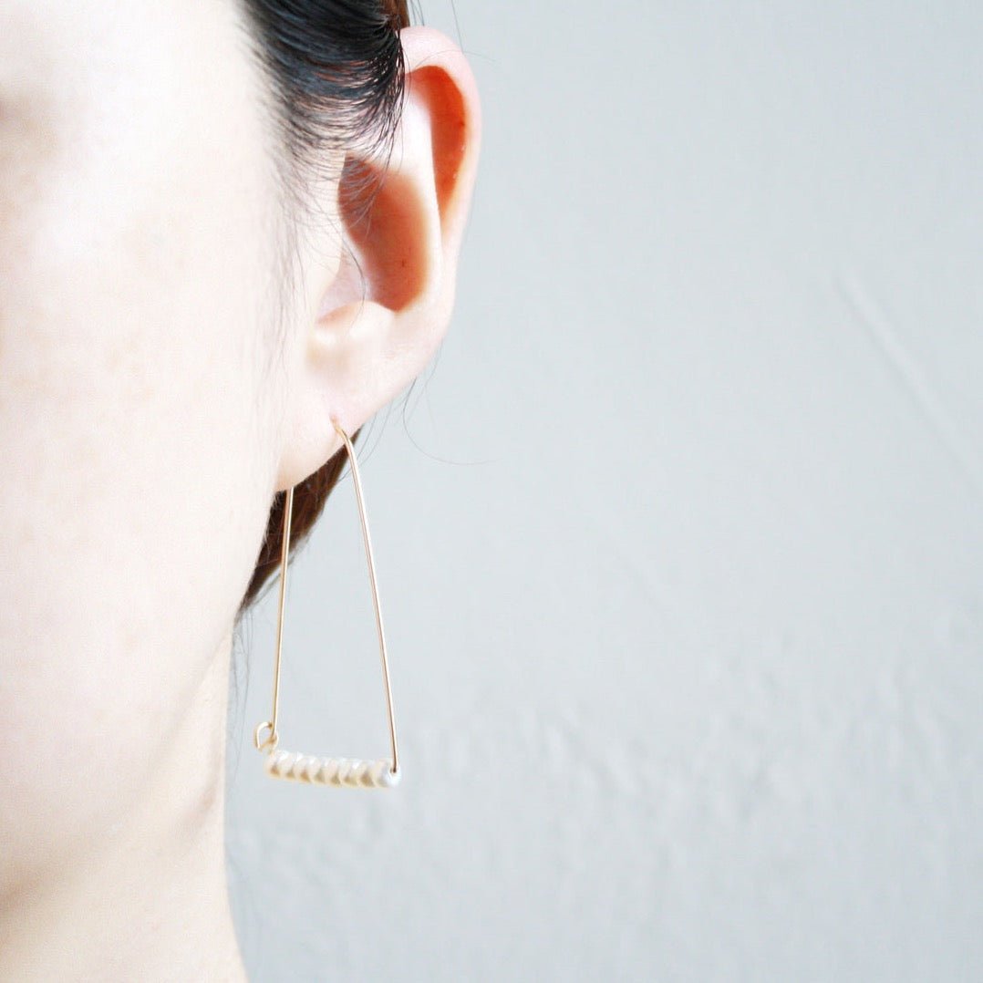 A model wears a wide gold tone arch shaped earring with a bar of freshwater pearls at the bottom. The Large Mountain Hoop earrings with Freshwater Pearls are designed by Hooks and Luxe handcrafted in Jackson Heights, NY.