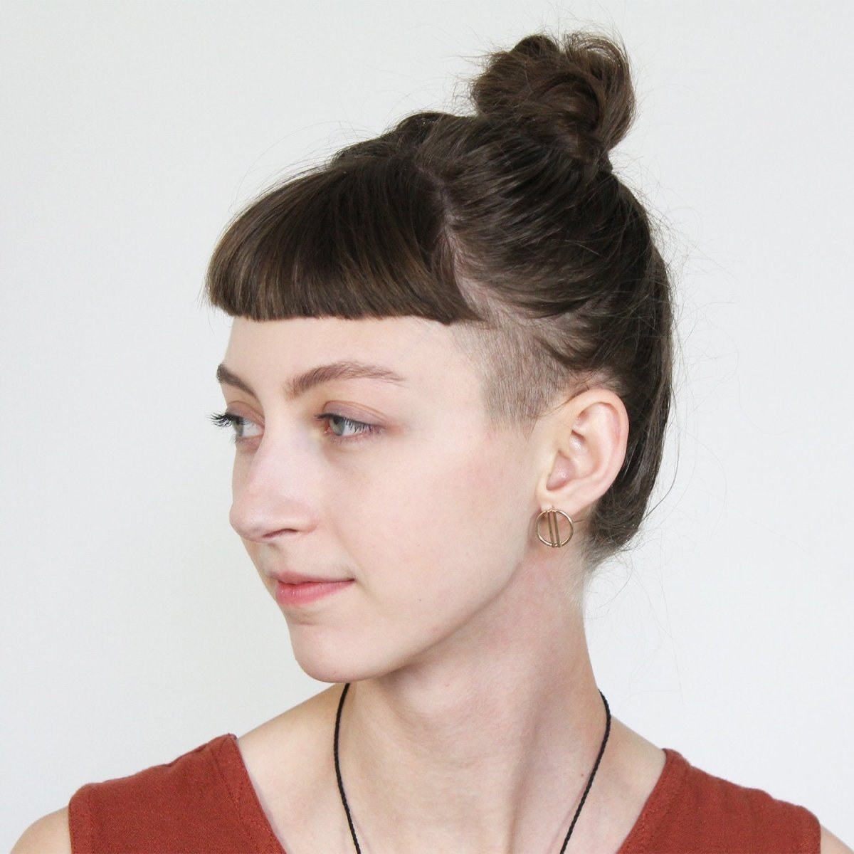 Betsy & iya bronze Liv stud earrings, pictured on the profile of a model with bangs and a topknot.
