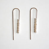 A gold tone u-shaped earring with multiple freshwater pearls stacked on one side. The Long arc Threader Earrings with Multiple Small Pearls are designed by Hooks and Luxe and handcrafted in Jackson Heights, NY.
