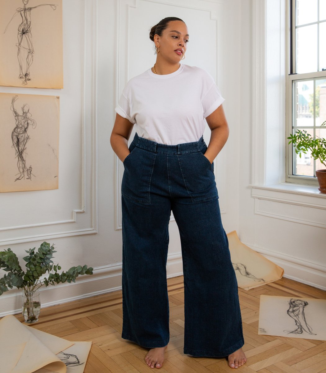 A model wears long wide legged denim pants with large front pockets. The Long Sabrina Jeans in Dark Indigo are designed by Loup and made in New York City, USA.