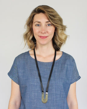 The brass and adjustable black leather Lumiko statement necklace, styled on a model with a chambray tunic and blonde hair.