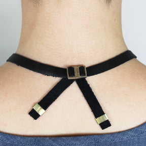 The back of the black leather Lumiko necklace, featuring an original betsy & iya cast-bronze buckle and shiny brass tubing accents, pictured on the back of a model's neck.