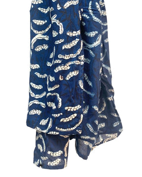 Dark blue scarf hangs in the air with cream flowers printed in a pattern against a white background. The Oversized Scarf in Etta is from designer Maelu.
