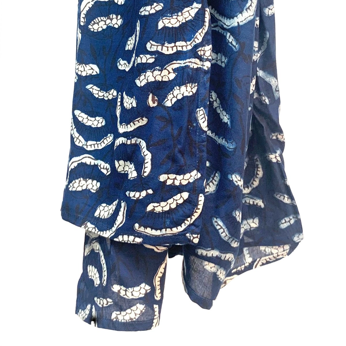 Dark blue scarf hangs in the air with cream flowers printed in a pattern against a white background. The Oversized Scarf in Etta is from designer Maelu.