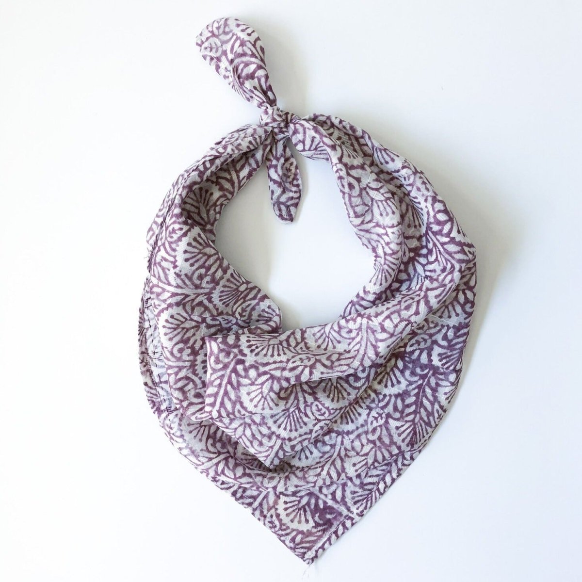 A purple and white patterned bandana, folded over and tied in a knot. Block printed by hand, the Lavender Bandana from Maelu is designed in Portland, Oregon and handmade in India.